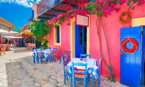 Kolorowa grecka wyspa Kefalonia. Stoliki kawiarniane pod kwitnącymi bugenwillami, niebieskie drzwi i koło ratunkowe.