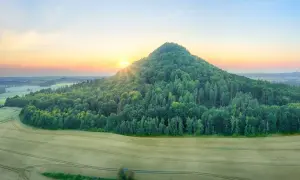Zalesione wzgórze o stożkowatym kształcie, przypominające wygasłe wulkany w Polsce, oświetlone zachodzącym słońcem.