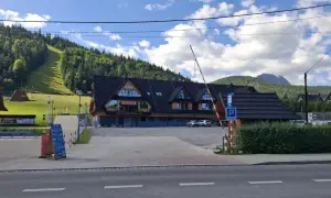 Parking pod Nosalem, z widokiem na górę i las. Restauracja z drewnianą elewacją, parking strzeżony.