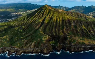 Widok z lotu ptaka na zielone wzgórza i ocean, gdzie leży Honolulu. W oddali widać zabudowania.