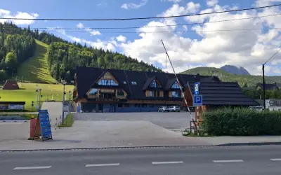 Parking pod Nosalem, z widokiem na górę i las. Restauracja z drewnianą elewacją, parking strzeżony.