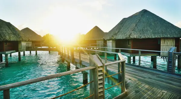 Zachód słońca nad turkusową wodą, drewniane pomosty i domki na palach – idealne wakacje na wyspach Bora Bora.