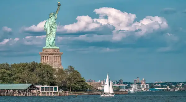 Statua Wolności i żaglówka na wodzie. Zastanawiasz się, ile kosztuje lot do USA z Polski?