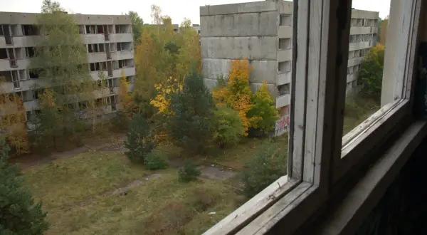 Pstrąże miasto widmo. Opuszczone bloki mieszkalne otoczone dziką przyrodą, zniszczone okna i puste balkony tworzą ponury krajobraz.