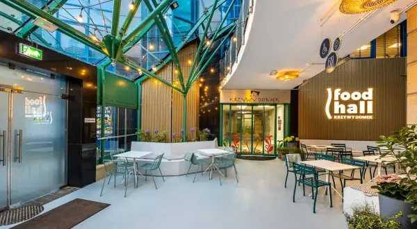 Nowoczesna strefa gastronomiczna "food hall Krzywy Domek Sopot" z zielonymi meblami i oświetleniem.