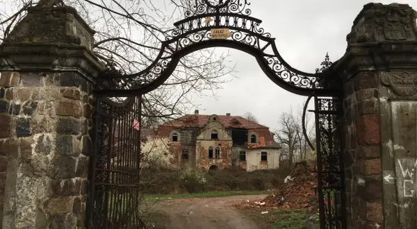 Zrujnowany pałac w glince, zniszczona brama i dziki ogród.