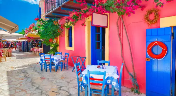 Kolorowa grecka wyspa Kefalonia. Stoliki kawiarniane pod kwitnącymi bugenwillami, niebieskie drzwi i koło ratunkowe.