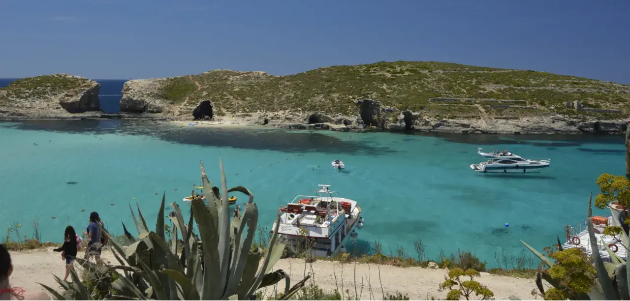 Malta co warto zobaczyć: Błękitna Laguna na Comino, z krystalicznie czystą wodą, łodziami i skalistymi klifami. Idealne miejsce na relaks.