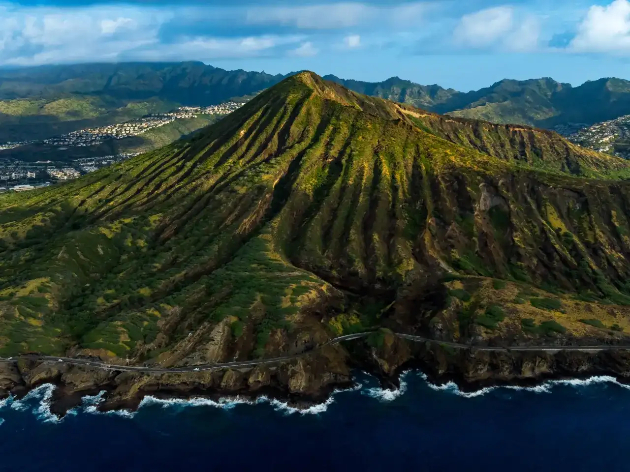 Widok z lotu ptaka na zielone wzgórza i ocean, gdzie leży Honolulu. W oddali widać zabudowania.