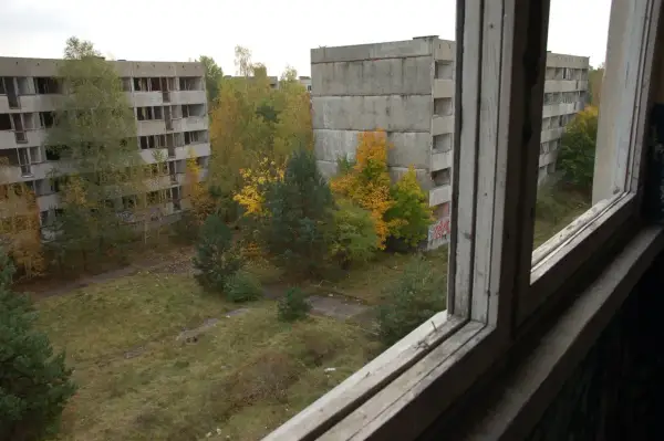 Pstrąże miasto widmo. Opuszczone bloki mieszkalne otoczone dziką przyrodą, zniszczone okna i puste balkony tworzą ponury krajobraz.