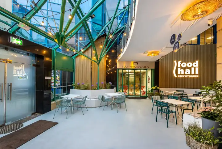 Nowoczesna strefa gastronomiczna "food hall Krzywy Domek Sopot" z zielonymi meblami i oświetleniem.